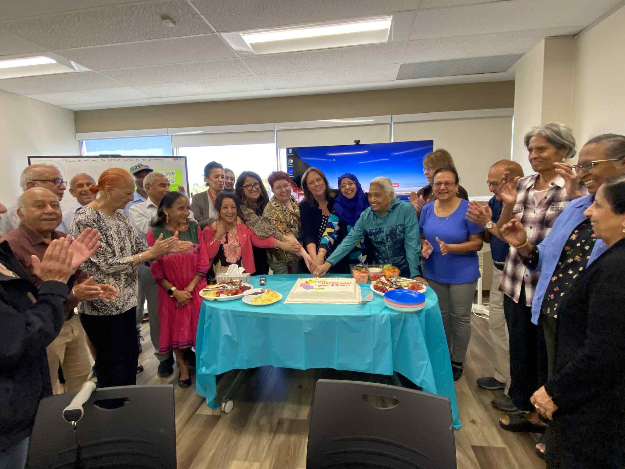 A group of NROCRC seniors gathered around a cake at a community celebration